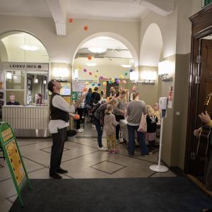 People have flocked to the event. A juggler is throwing balls. A musician plays the guitar.
