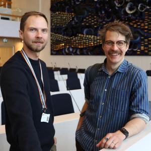 Mikael and Henrik pictured in the council chamber. In the background, a dark blue Pansy Sea artwork in dark blue and gold.