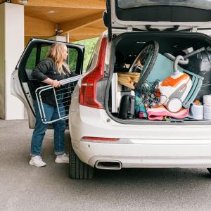 Henkilö lastaa autoa täyteen tavaraa ja auton takakontti on auki.