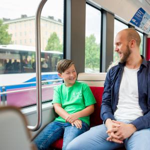 Mies ja poika istuvat bussissa, jonka ikkunasta näkyy toinen bussi.