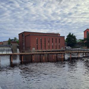 The photo shows a lightweight bridge below the red-brick power plant at Tammerkoski Rapids.