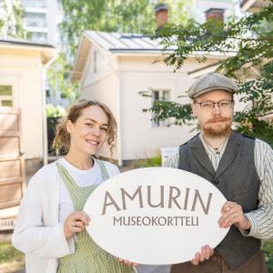 Kaksi vanhanaikaisiin asuihin pukeutunutta henkilöä pitelee käsissään Amurin museokortteli -kylttiä.