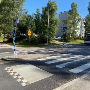 Suojatie ja hidasteet kuvattu kesällä ja bussi näkyy taustalla lähestyvän suojatietä.