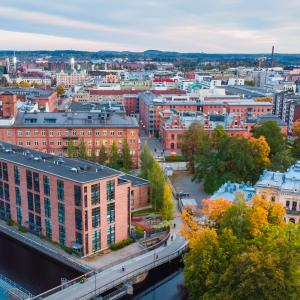 Ilmakuva Tampereen keskustasta, jossa näkyvät Tammerkosken punatiiliset tehdasrakennukset, syksyinen puistoalue ja kaupungin siluetti.