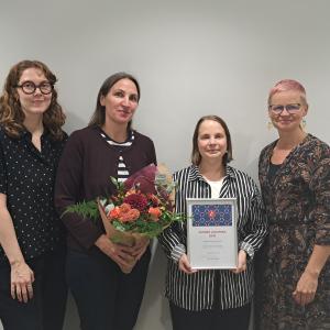 Lastenkirjainstituutin neljän työntekijää. Yhdellä on kädessään kukkakimppu, toisella diplomi. 
