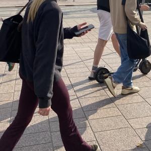 Ihmisiä kävelemässä keskustassa ja edustalla henkilö kävelee puhelin kädessä.