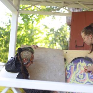 Two people are carrying sheets of plywood for an art project.