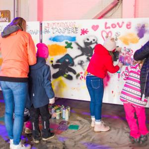 Adults and children are painting a large work of art together. 