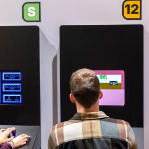 Kaksi henkilöä istuu Pelimuseossa pelipisteiden äärellä pelaamassa.
