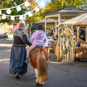 A woman is leading a pony, with a child sitting on its back, wearing a riding helmet.