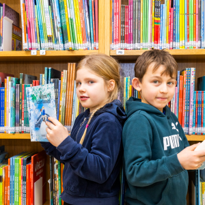 Two people reading books in front of a bookcase.