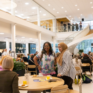 There are lots of people sitting at tables having a coffee in a large, bright hall. 