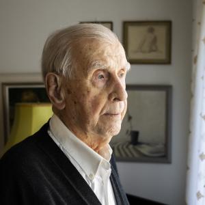 A person looks out of a window, with paintings visible in the background.