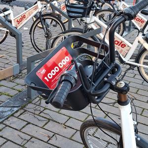 Kaupunkipyöriä pyöräasemalla. Etualalla olevan pyörän koriin on kiinnitetty miljoonannesta matkasta kertova kyltti.