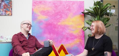 Kaksi ihmistä istuu kahvikupit kädessä vastakkain. 