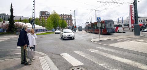 A man and a woman at a pedestrian crossing, a car and a tramway coming.