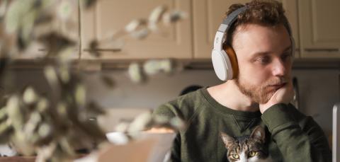Mies istuu keittiössä ja kuuntelee kuulokkeilla kissa sylissään.