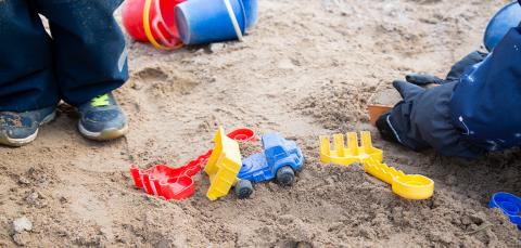 Hiekalla leikkiharavia ja kuorma-auto. Kaksi lasta leikkimässä.
