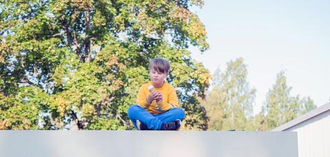 Jäätelöä syövä poika istumassa Satajalka-veistoksen päällä.