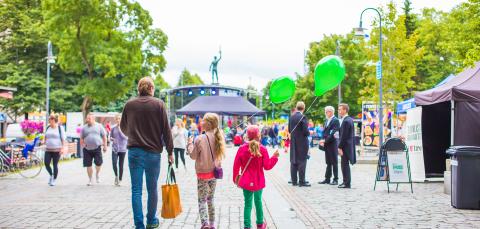 Aikuinen ja kaksi lasta Hämeenpuistossa, lapsilla vihreät ilmapallot kädessä. Taustalla ihmisjoukkoa.