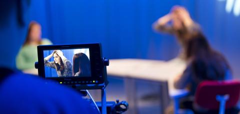 Videokuvaus on käynnissä. Etualalla näkyy kuva kameran ruudulta ja taustalla näkyy nuori nainen, jota kuvataan.