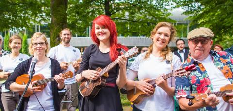 Hymyileviä ukulelensoittajia puistossa.