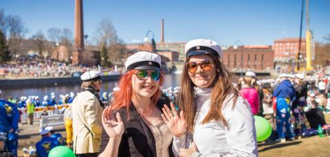 Two students wearing Finnish student caps waving hands at Koskipuisto.