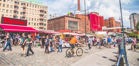 Ihmisiä kävellen ja pyörällä Laukontorilla. Aurinko paistaa.