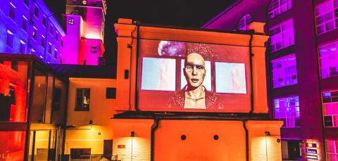 Kuva valotaaidetapahtuma Projiosta, runsaasti eri värejä rakennusten seinissä, keskellä ihmisen kuva