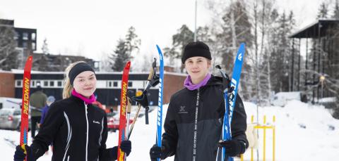 Two people standing and holding skis in hands at snowy Kauppi Sports Park.