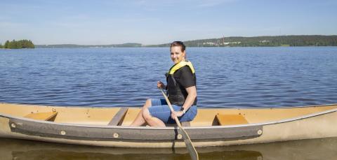 A person is paddling in a canoe in a sunny lakeside scenery.