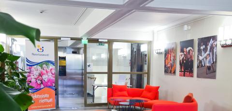 Vaaleassa aulatilassa on kirkkaanpunaiset sohvat. Seinille on ripustettu suurikokoisia valokuvia. Tilassa on myös suuri viherkasvi.