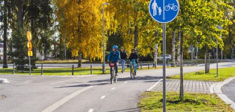 Kolme pyöräilijää ajaa pyörätiellä syksyllä.