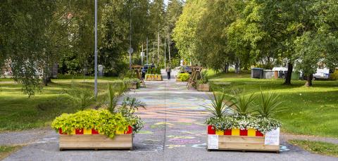 Kukkalaatikoita katkaisemassa katua autoliikenteeltä ja taustalla katumaalaus.
