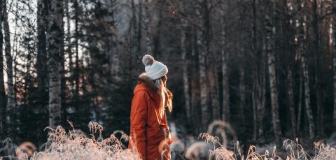 Nainen katsoo koivumetsää lumisessa maisemassa.