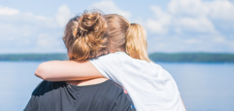 Kaksi henkilöä istuu lähekkäin ja katsoo kauas järvimaisemaa.