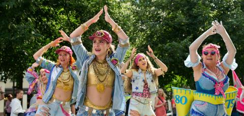 Värikkäästi pukeutuneita naisia tanssimassa kädet ylhäällä pään päällä.