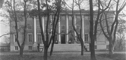 Mustavalkoisessa valokuvassa on iso klassinen rakennus keskellä puistoa.