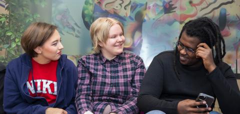 Kolme nuorta istumassa, keskimmäisellä kädessä kirja.