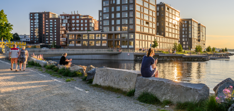 Ihmisiä kävelemässä ja istumassa järven äärellä. Taustalla kerrostaloja.