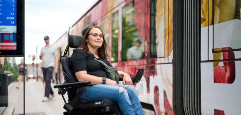 Pyörätuolissa istuva henkilö odottaa laiturilla pääsyä ratikkaan.