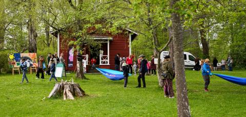 Ihmisiä vihreässä puistossa, jossa on värikkäitä taideteoksia. Osa ripustaa riippumattoja. 