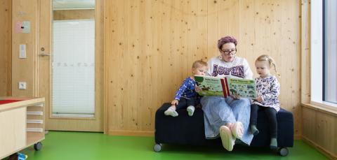 Aikuinen lukee kirjaa kahdelle lapselle.