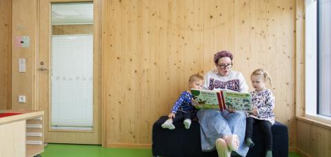 Aikuinen lukee kirjaa kahdelle lapselle.
