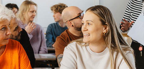 Kaksi henkilöä juttelee. He istuvat pulpeteissa.