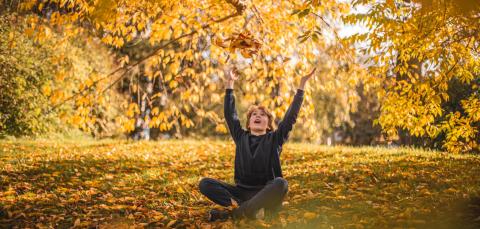 A child is sitting on the ground, tossing autumn leaves into the air.