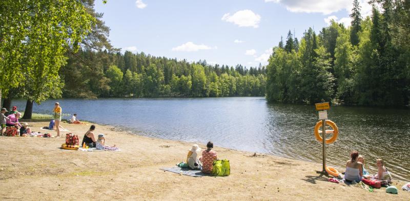 Ihmisiä uimarannalla istumassa hiekalla aurinkoisena päivänä.