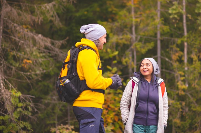 Two walkers in an autumnal forest, with rucksacks on their backs.