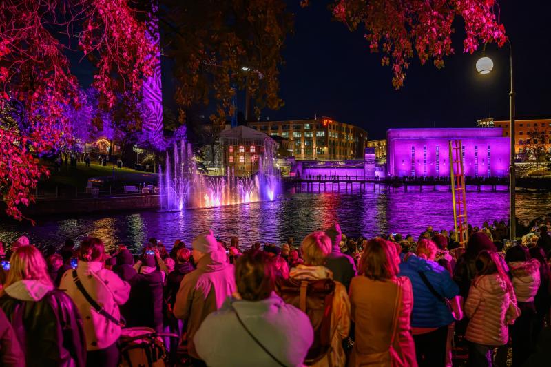 A gathering of people watching a Dancing waters show at the Tammerkoski at night.
