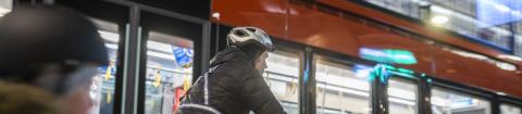 An adult and a child cycling on the street in winter. They are wearing reflectors, lights and helmets. A tram passes them. 